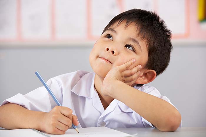 Boy with a pen in his hand looks up as if thinking or imagining what he will be writing