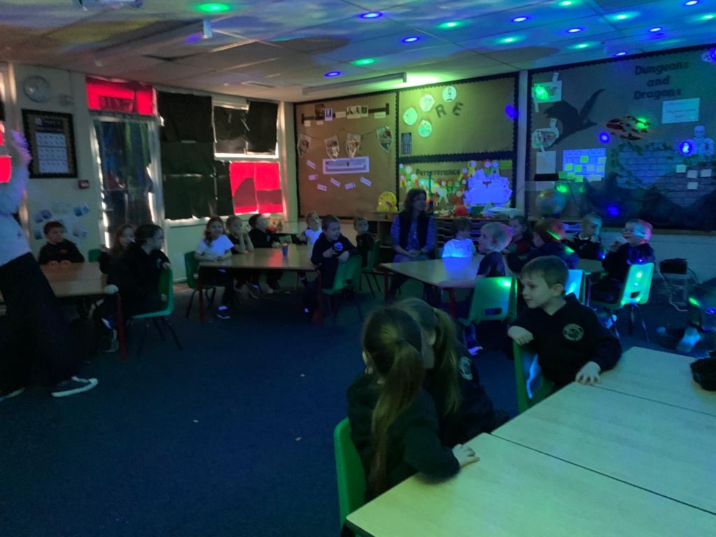 Children seated at desks in a classroom as lights illuminate the space in different colours.